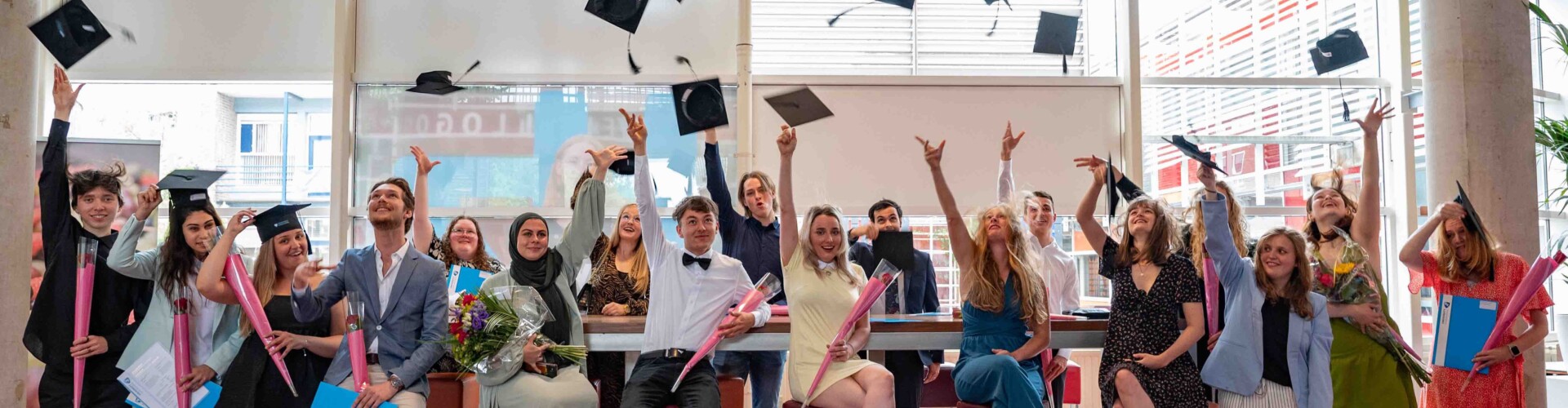Groep studenten die na de diplomeringen hun hoedje in de lucht gooien